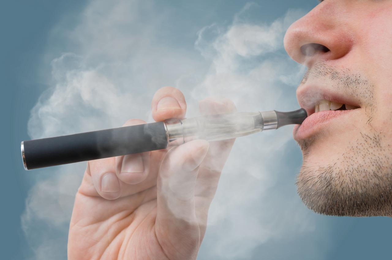 A close-up of someone using a vape pen with teeth visible.