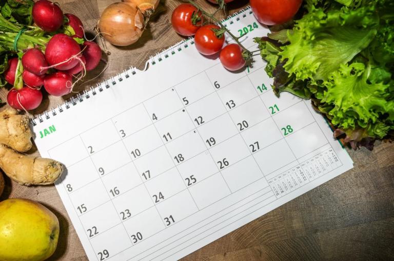Calendar on wood table surrounded by fruits and veggies